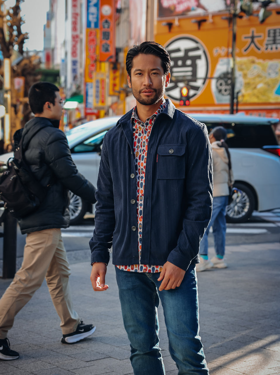 A Fish Named Fred men's Rib overshirt in Navy, worn by a model on a neon-signed shopping street