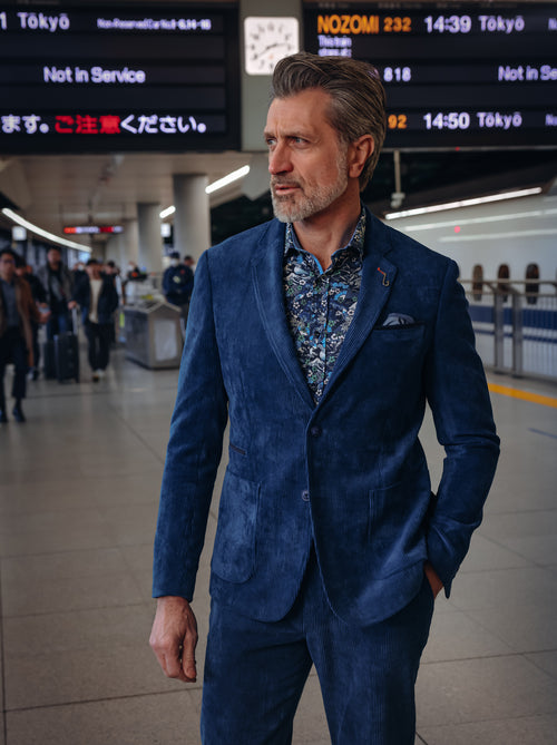 A Fish Named Fred men's Rib blazer in Night Sky Blue, worn by a model walking through a station concourse