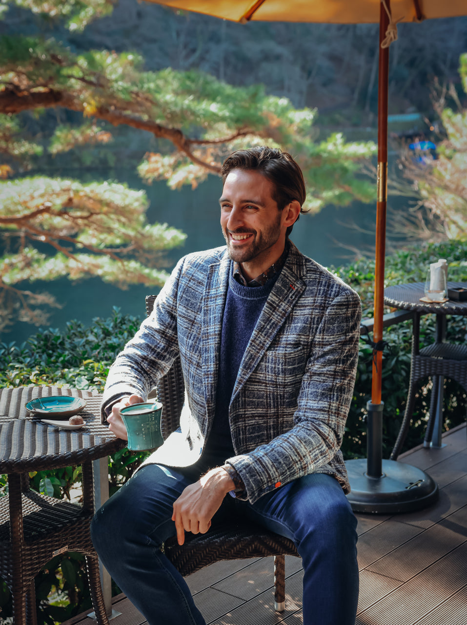 A Fish Named Fred men's Fancy Check blazer in Jeans Blue, worn by a model at a garden cafe under a parasol, AW26 lookbook