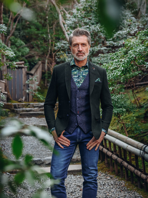 A Fish Named Fred men's Herringbone blazer in Dark Green, worn by a model on a garden path