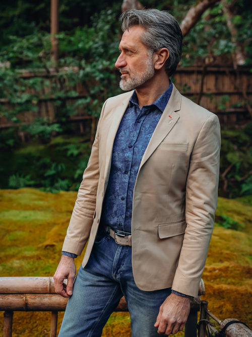A Fish Named Fred men's Fancy Embroidery blazer in Sand, worn by a model in a mossy garden