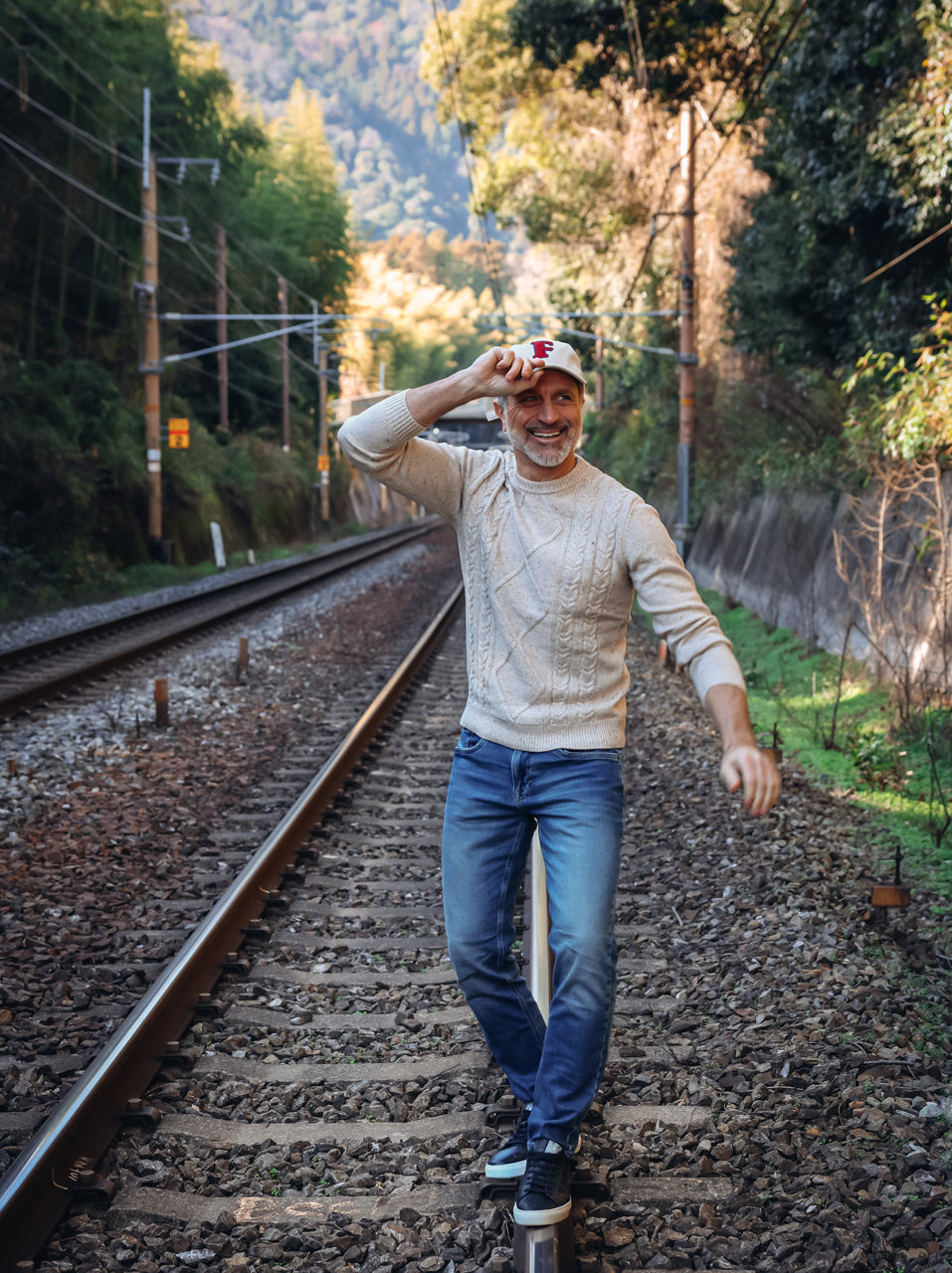 A Fish Named Fred men's Rib cap in Off-White, worn by a model walking along railway tracks