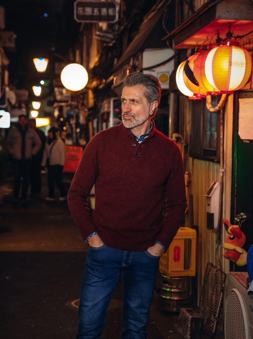 A Fish Named Fred men's Knitted jumper in Burgundy, worn by a model in a lantern-lit alley at night