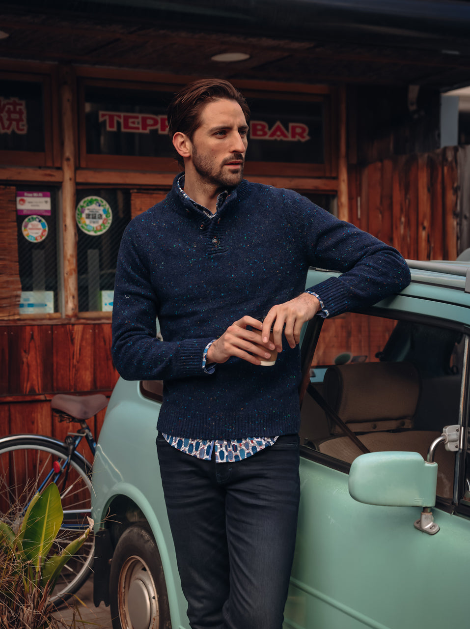 A Fish Named Fred men's Knitted jumper in Navy, worn by a model leaning on a vintage van