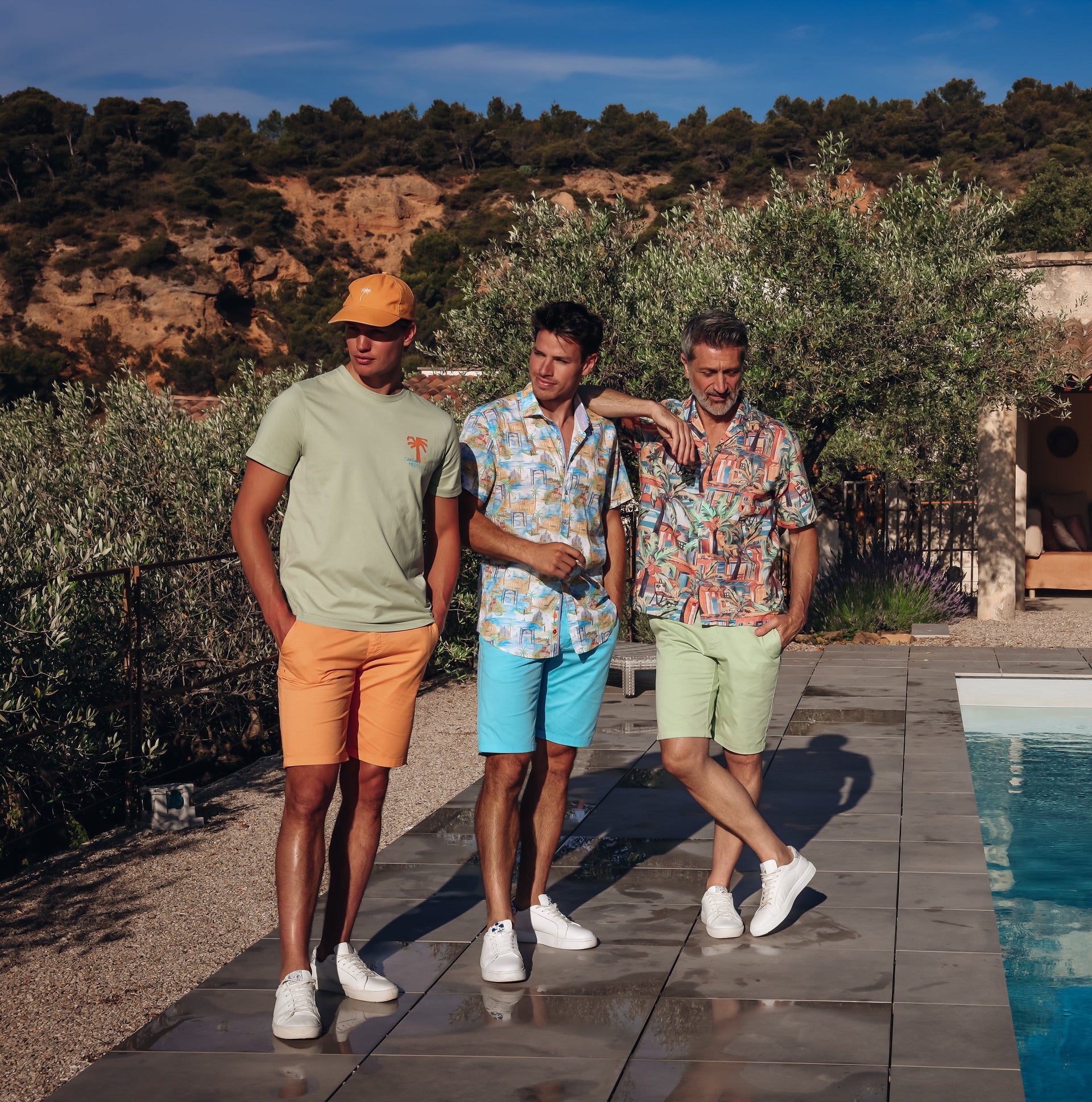 Three men standing by a poolside with a scenic background